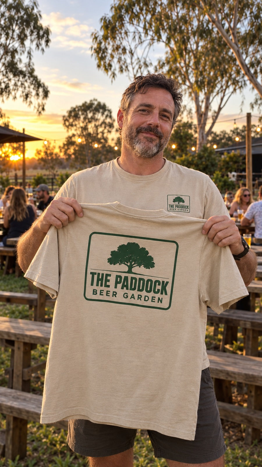 The owner holding up a tan tee with The Paddock stamp on the back, in the beer garden