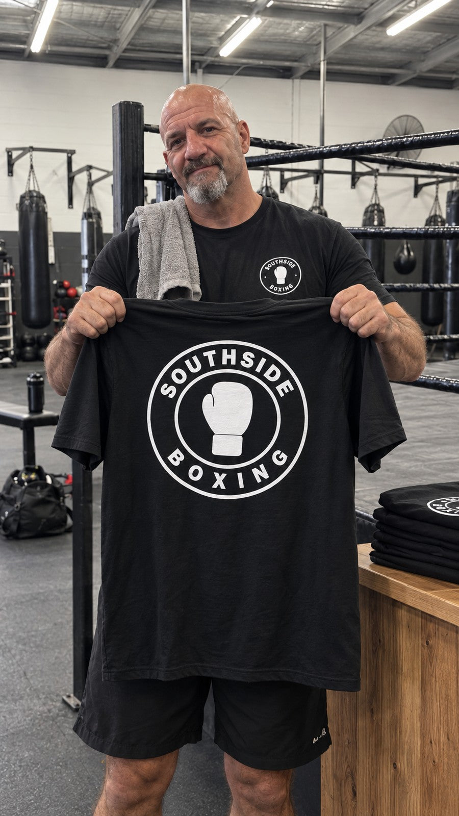 The gym owner holding up a black tee with the Southside Boxing logo on the back