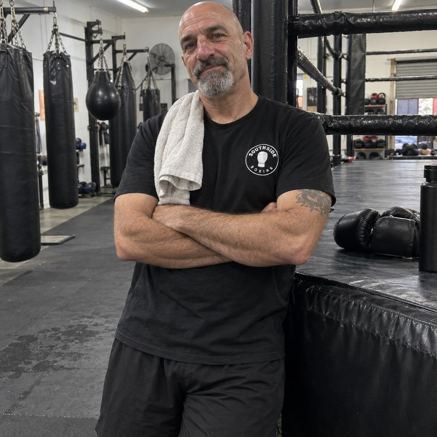 The gym owner by the ring in a tee with the gym logo on the chest